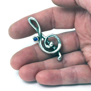 
            
                Load image into Gallery viewer, Treble Clef brooch in Sterling silver set with lab grown sapphire
            
        